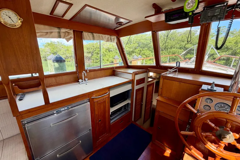 Slide: The Image of 1983 Grand Banks 32 Sedan interior with wooden helm, kitchen, and large windows. - 27