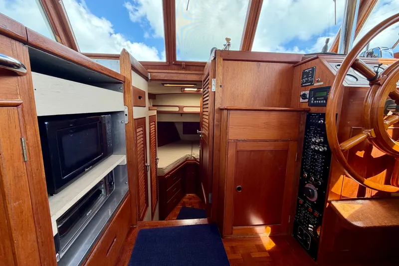 Slide: The Image of 1983 Grand Banks 32 Sedan interior with wooden helm, microwave, and cozy cabin space. - 37