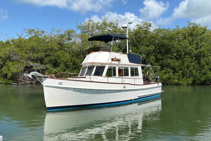 Slide: The Image of 1983 Grand Banks 32 Sedan boat on calm water, surrounded by lush greenery. - 4