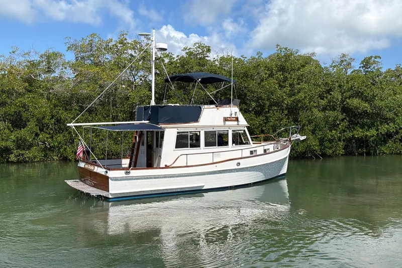 Slide: The Image of 1983 Grand Banks 32 Sedan boat on calm water, surrounded by lush greenery. - 5