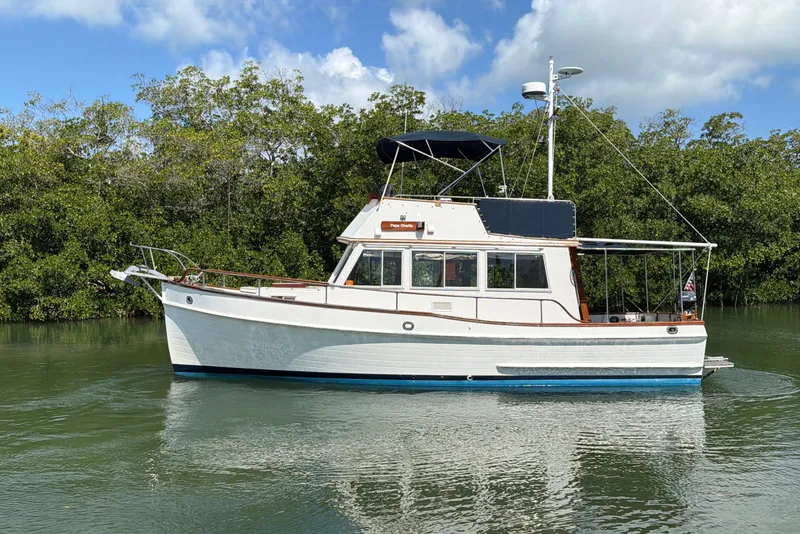 Slide: The Image of 1983 Grand Banks 32 Sedan boat on calm water with lush greenery background. - 7