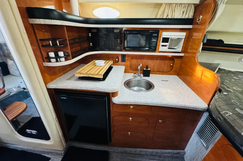 Slide: The Image of 2002 Rinker Fiesta Vee 342 boat interior with kitchenette, featuring sink, microwave, and wooden cabinetry. - 42