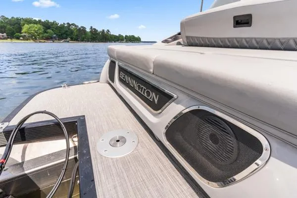Slide: The Image of 2023 Bennington QX 25 QXSBA boat on a lake, featuring sleek design and speaker system. - 15