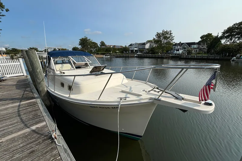 The Image of 2005 Mainship Pilot 30-II Sedan docked by a serene waterfront with American flag. - 0