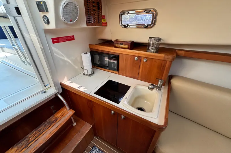 Slide: The Image of 2005 Mainship Pilot 30-II Sedan galley with sink, stove, and wooden cabinetry. - 26