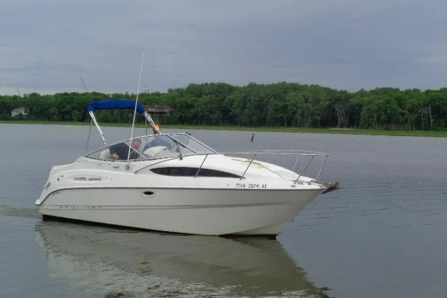 Slide: The Image of 2000 Bayliner 2455 Ciera Sunbridge cruising on a calm lake with forested shoreline. - 2
