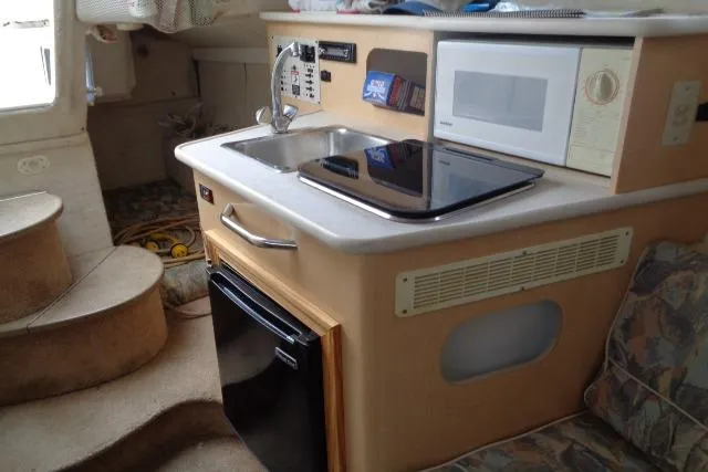 Slide: The Image of 2000 Bayliner 2455 Ciera Sunbridge interior with kitchenette, microwave, and compact fridge. - 26