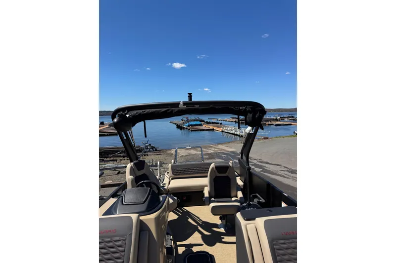 Slide: The Image of 2026 Harris Sunliner 230 Sport boat at a lakeside dock under clear blue skies. - 11