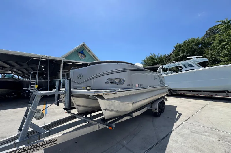 Slide: The Image of 2021 Avalon LSZ 2485 QL pontoon boat on trailer at marina under clear blue sky. - 4