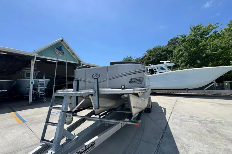 Slide: The Image of 2021 Avalon LSZ 2485 QL pontoon boat on trailer at marina under clear blue sky. - 5