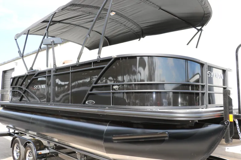 Slide: The Image of 2025 Sylvan Mirage X3 pontoon boat with black exterior and canopy on trailer. - 4