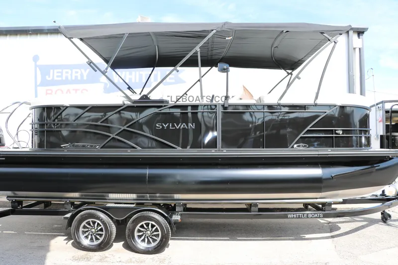 Slide: The Image of 2025 Sylvan Mirage X3 pontoon boat on trailer, black exterior, under canopy. - 7
