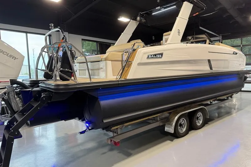 Slide: The Image of 2025 Balise Helix 26 L boat on trailer in showroom with blue underglow lighting. - 4