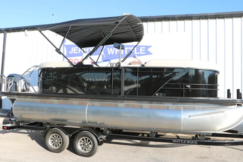 The Image of 2025 Sylvan Mirage X1 pontoon boat on trailer, black canopy, parked outside. - 0