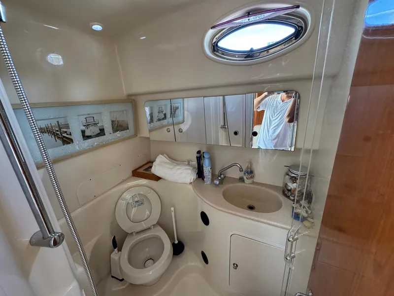 Slide: The Image of Bathroom interior of 2002 Sea Ray 360 Sundancer yacht, featuring sink, toilet, and porthole window. - 26