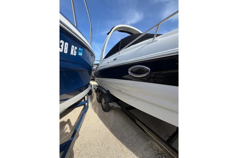 Slide: The Image of 2020 Crownline 286 SC boat on trailer, parked beside another vessel under clear sky. - 22