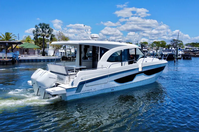 Slide: The Image of 2021 Beneteau Antares 11 cruising on a sunny day, surrounded by palm trees and docks. - 2