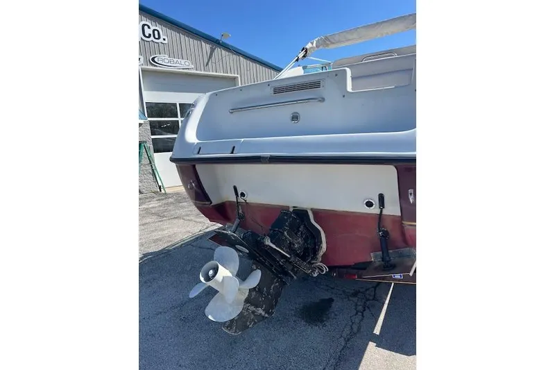 Slide: The Image of 1997 Crownline 250 CR boat stern view with propeller, parked near a building. - 14
