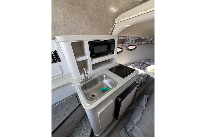 Slide: The Image of 1997 Crownline 250 CR boat interior with kitchenette, sink, microwave, and cozy seating area. - 6