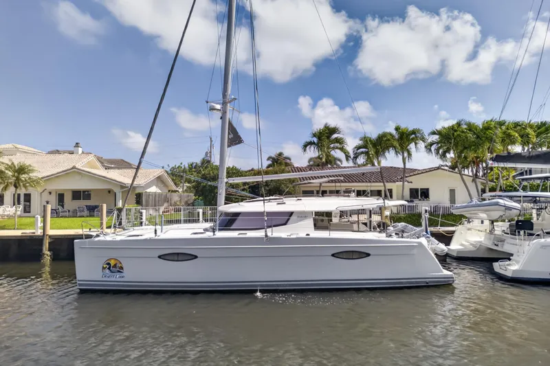 Slide: The Image of 2015 Fountaine Pajot Helia 44 catamaran docked by waterfront homes, under a clear blue sky. - 1