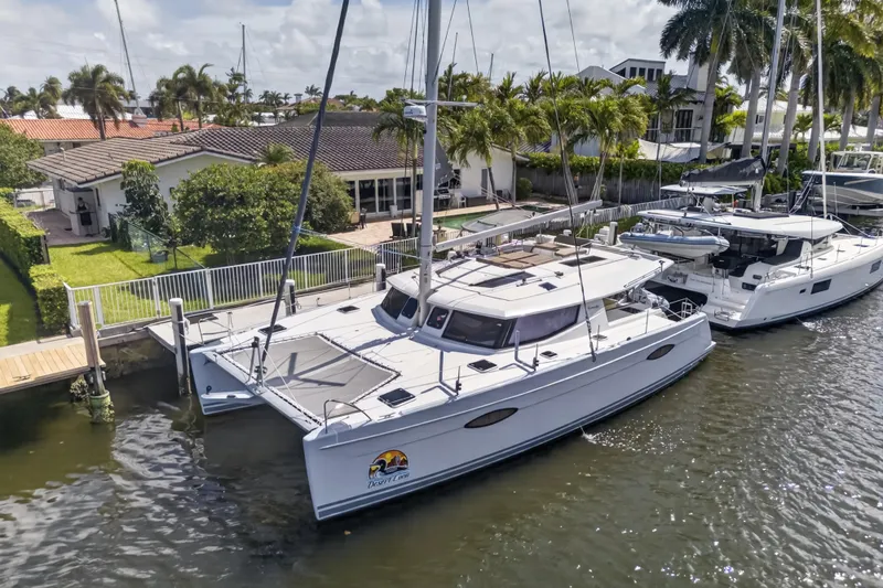 Slide: The Image of 2015 Fountaine Pajot Helia 44 catamaran docked by waterfront homes, surrounded by palm trees. - 2