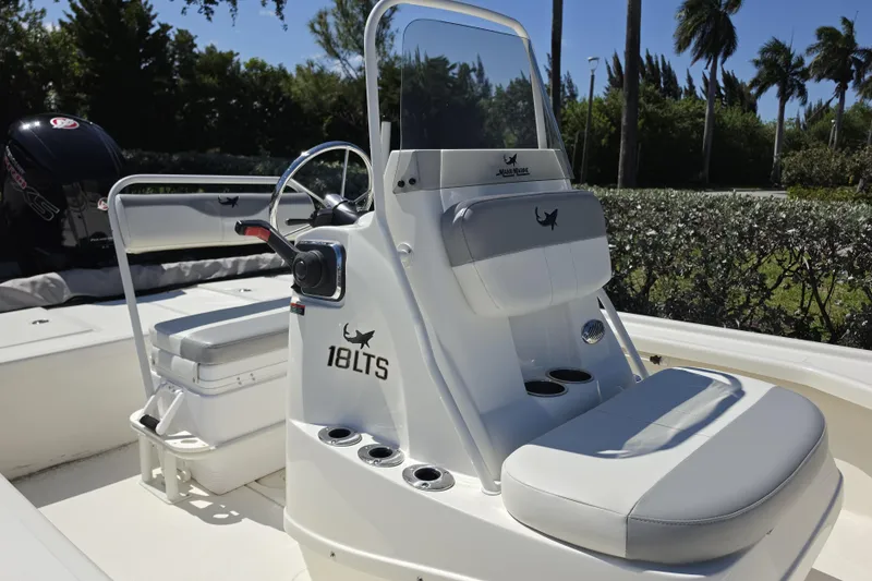 Slide: The Image of 2023 Mako 18 LTS boat interior with steering console and seating, surrounded by lush greenery. - 8