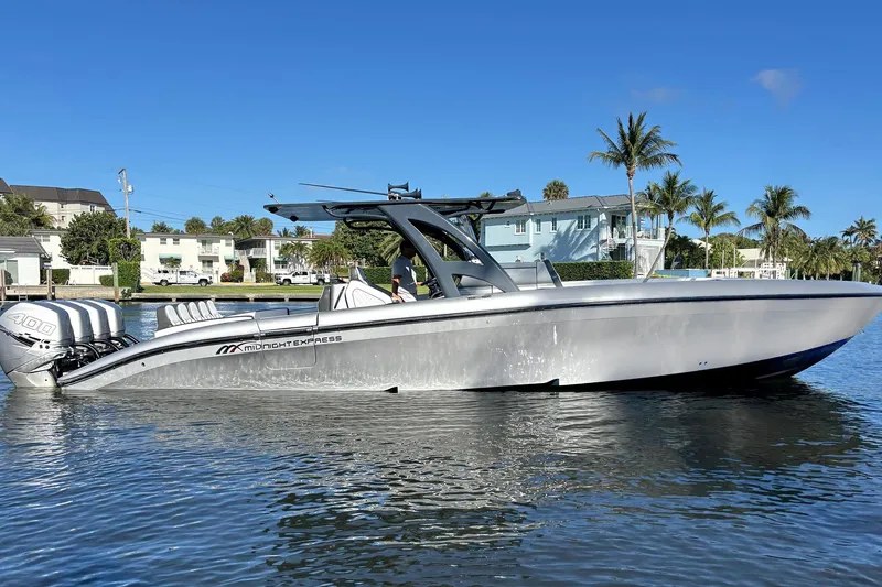 Slide: The Image of 2021 Midnight Express 37 Open boat on calm water, with palm trees and houses in the background. - 14
