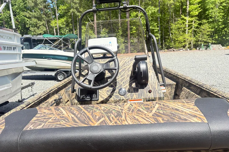 Slide: The Image of 2022 Lowe Roughneck 1860CC boat with camo interior, steering wheel, and control panel in a wooded area. - 5