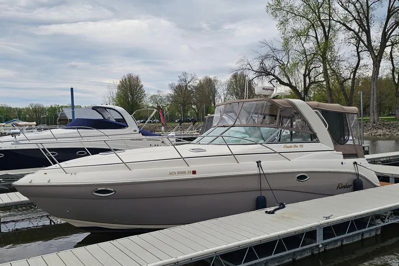 The Image of 2004 Rinker Fiesta Vee 312 boat docked at marina, surrounded by trees and other boats. - 1