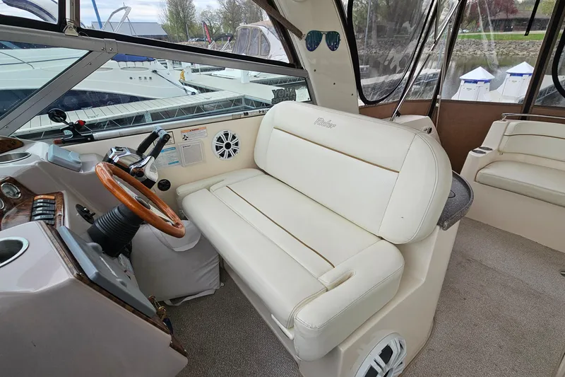 Slide: The Image of 2004 Rinker Fiesta Vee 312 boat interior with white seating and wooden steering wheel. - 11