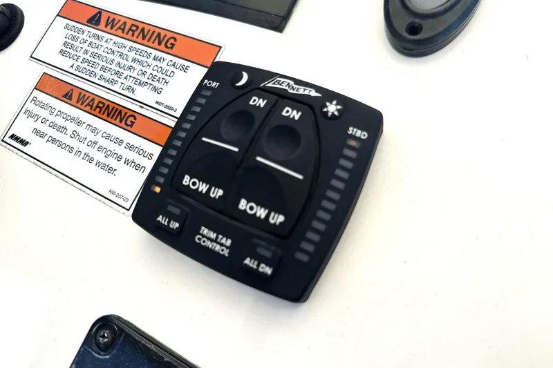 Slide: The Image of 2023 Pathfinder 2200 TRS boat control panel with warning labels and trim tab controls. - 11
