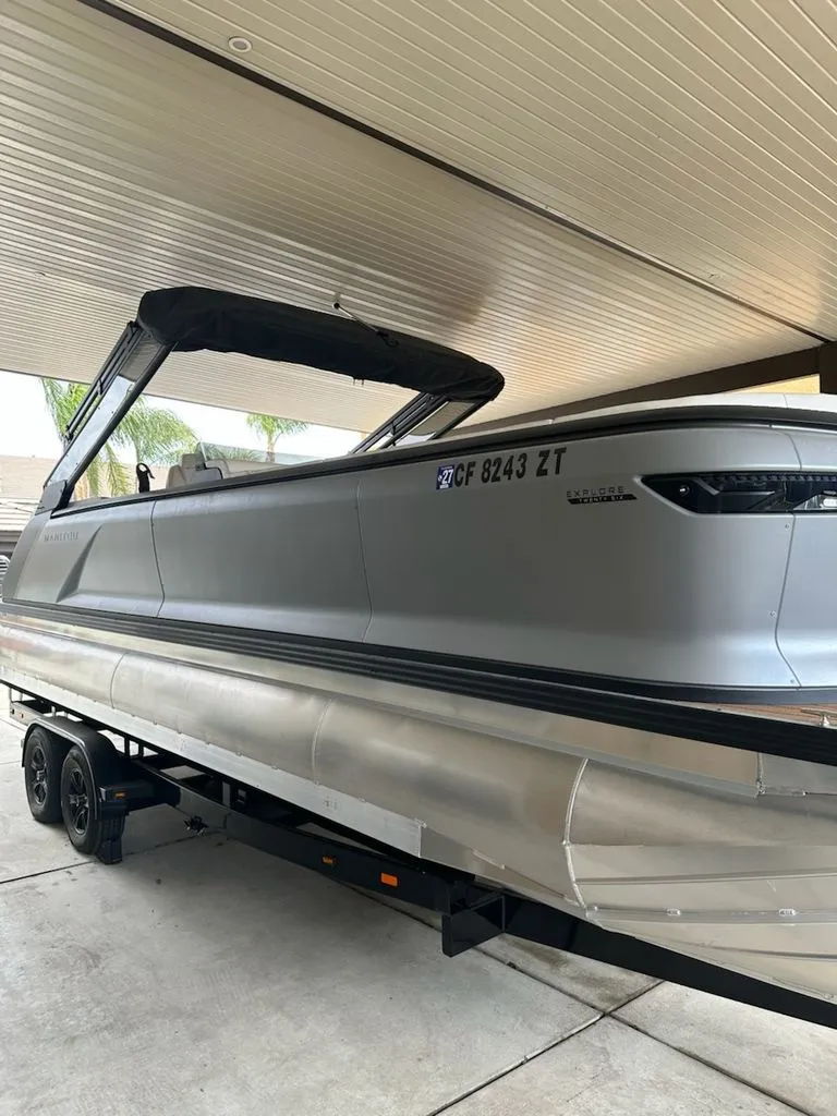 Slide: The Image of 2024 Manitou Switchback pontoon boat on trailer under carport. - 2