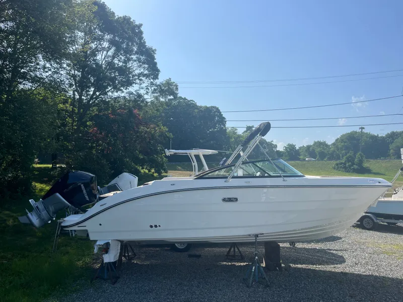 Slide: The Image of A 2026 Sea Ray SDX 250 Outboard is on a gravel lot, surrounded by trees. - 0