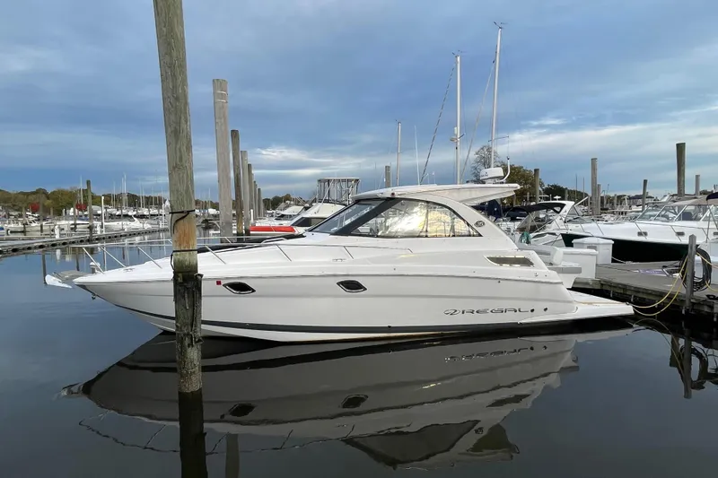 The Image of 2012 Regal 35 Sport Coupe yacht docked in a marina, reflecting on calm water. - 0