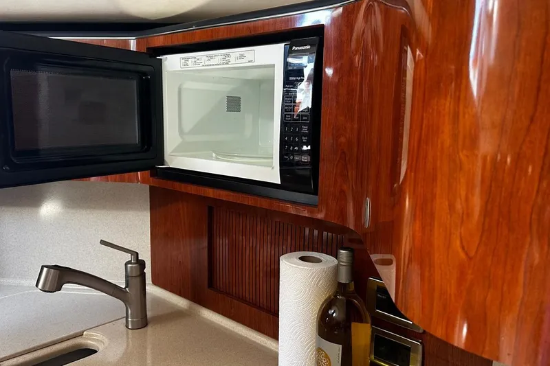 Slide: The Image of 2004 Sea Ray 380 Sundancer galley with open microwave, sink, and wooden cabinetry. - 10