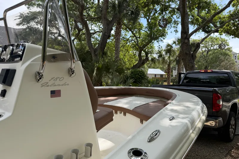 Slide: The Image of 2023 Pioneer 180 Islander boat on trailer, parked near trees and a pickup truck. - 11