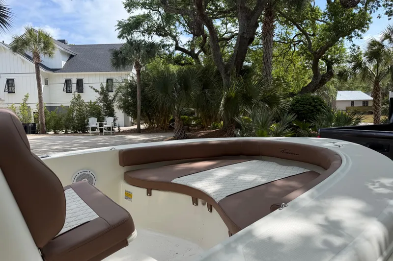 Slide: The Image of 2023 Pioneer 180 Islander boat interior with brown seating, surrounded by lush greenery. - 12