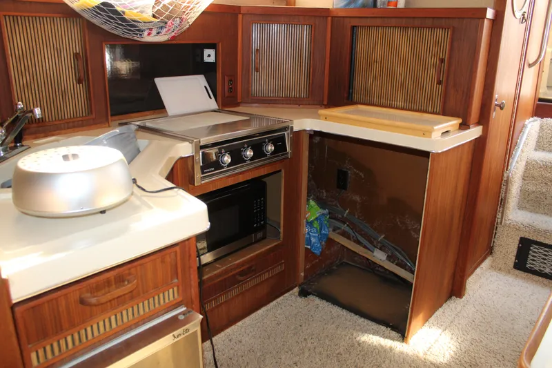 Slide: The Image of 1986 Searay 340 Express yacht kitchen with stove, microwave, and wooden cabinetry. - 16