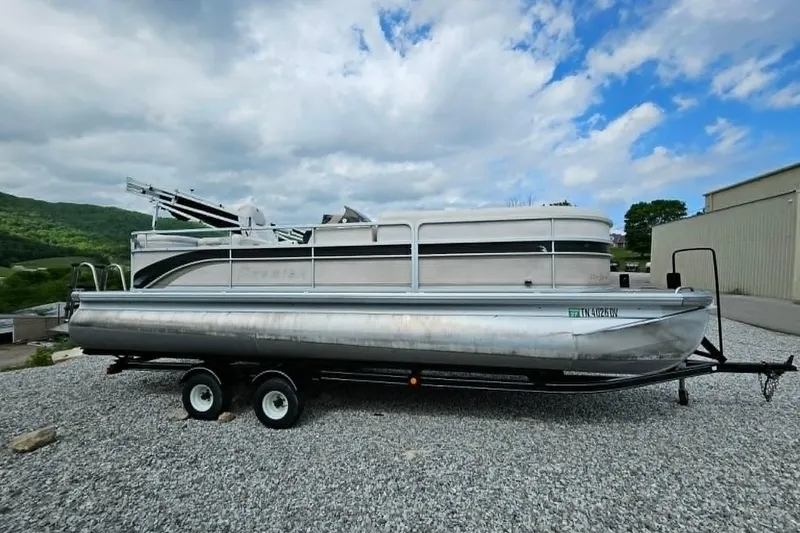 The Image of 2007 Premier 225 Legend RE pontoon boat on trailer, parked on gravel with cloudy sky backdrop. - 0