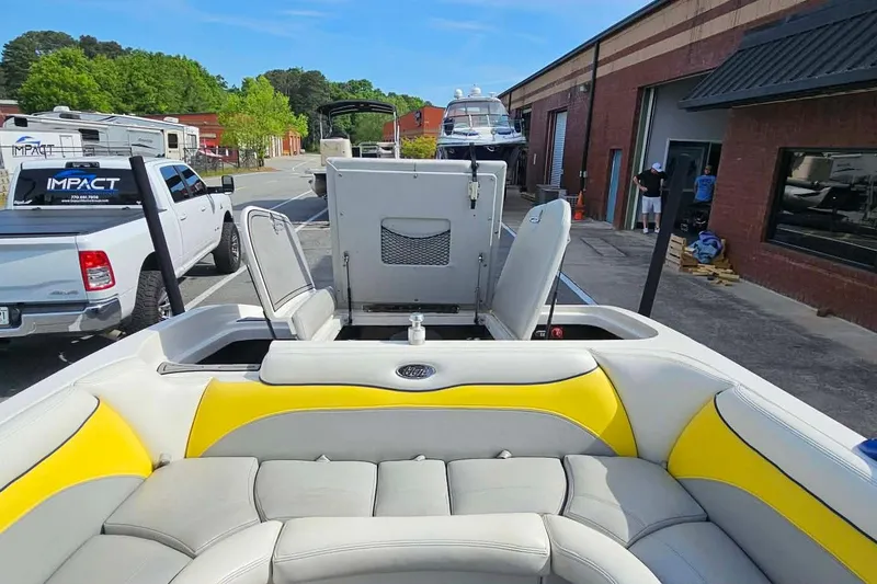 Slide: The Image of 2006 Tigé 22Ve boat interior with yellow and gray seating, parked near a workshop. - 14