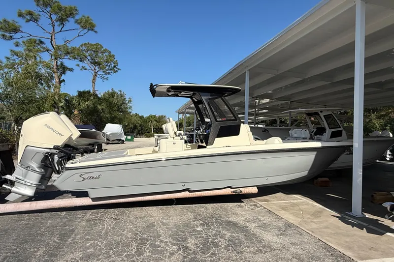 Slide: The Image of 2026 Scout 281 XSS boat with Mercury engine, parked under a canopy on a sunny day. - 3