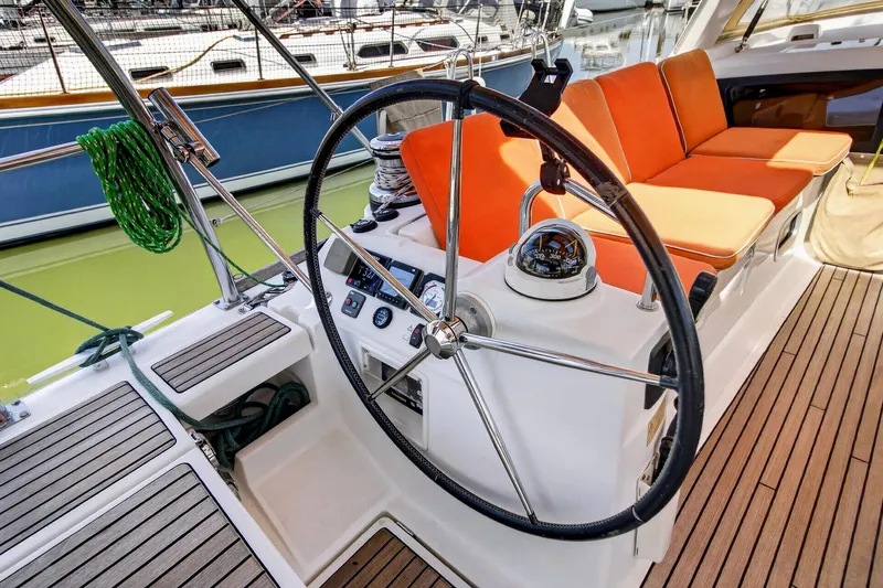 Slide: The Image of Steering wheel and seating area of 2012 Beneteau Oceanis 48 sailboat with orange cushions. - 20