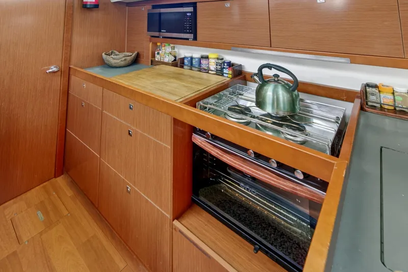 Slide: The Image of Galley kitchen in 2012 Beneteau Oceanis 48 yacht with stove, microwave, and wooden cabinetry. - 40