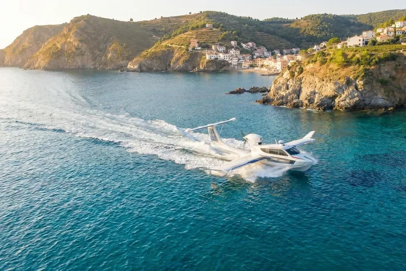 Slide: The Image of Seaplane Aron M 80 (2026) cruising near scenic coastal cliffs and village. - 2