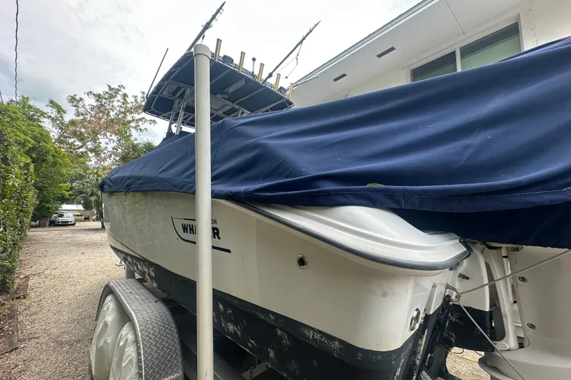 Slide: The Image of 2004 Boston Whaler 270 Outrage boat covered, parked on a trailer in a driveway. - 10