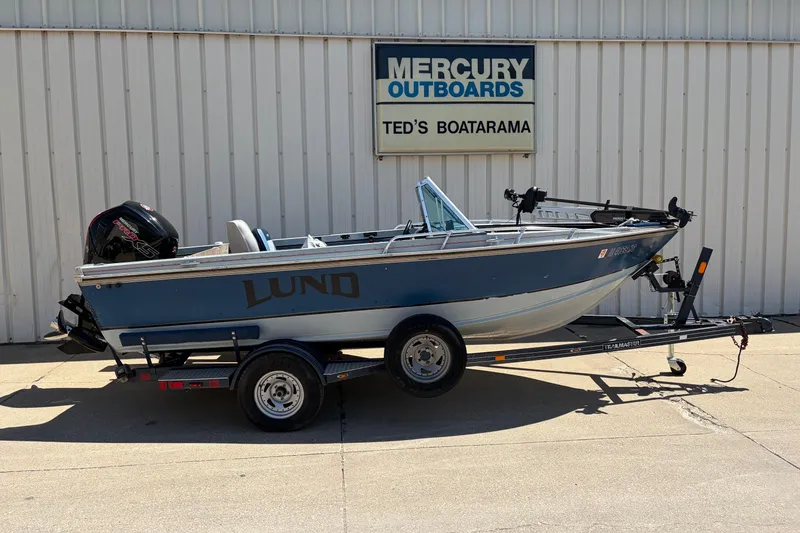 The Image of 1991 Lund 1750 Tyee boat on trailer, parked outside Mercury Outboards dealership. - 0