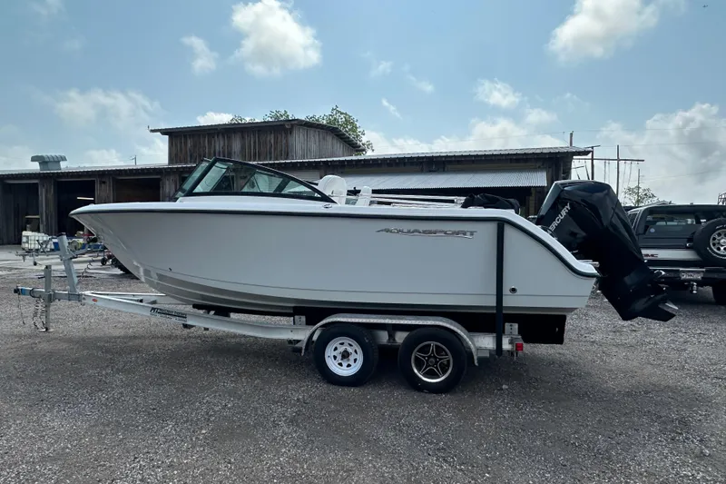 Slide: The Image of 2024 Aquasport 2200 Dual Console boat on trailer, parked outdoors. - 2
