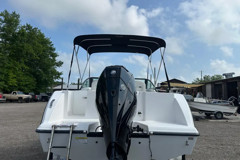 Slide: The Image of 2024 Aquasport 2200 Dual Console boat with outboard motor and canopy, parked outdoors. - 44