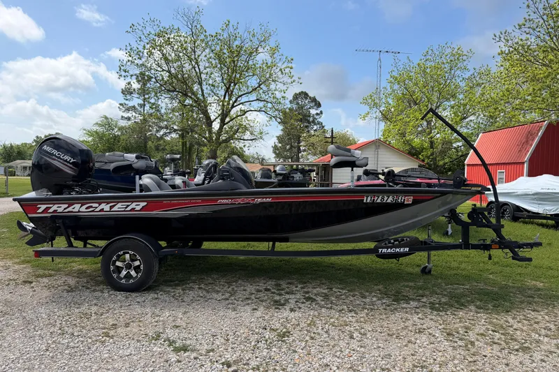 The Image of 2018 Bass Tracker boat on trailer, parked outdoors with trees and buildings in the background. - 1
