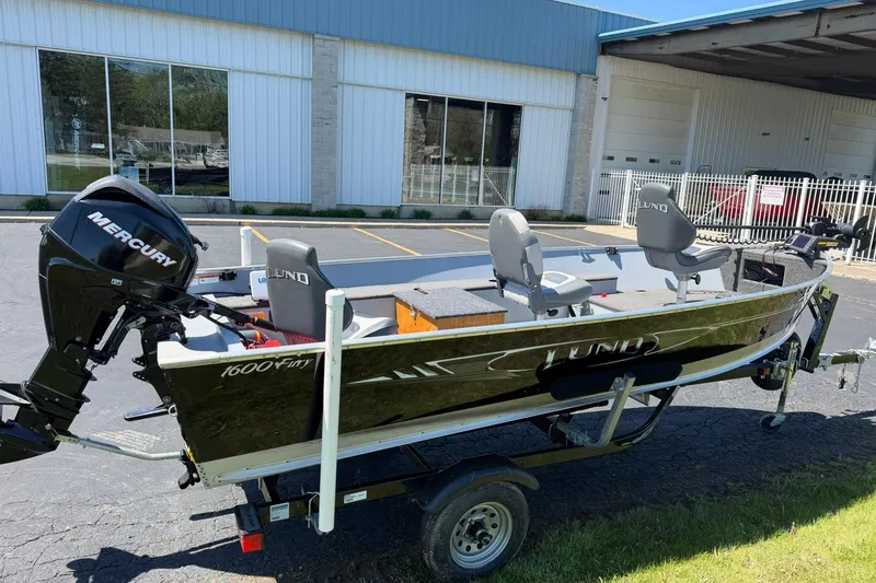 Slide: The Image of 2013 Lund 1600 Fury Tiller boat with Mercury engine on trailer, parked outside a building. - 2